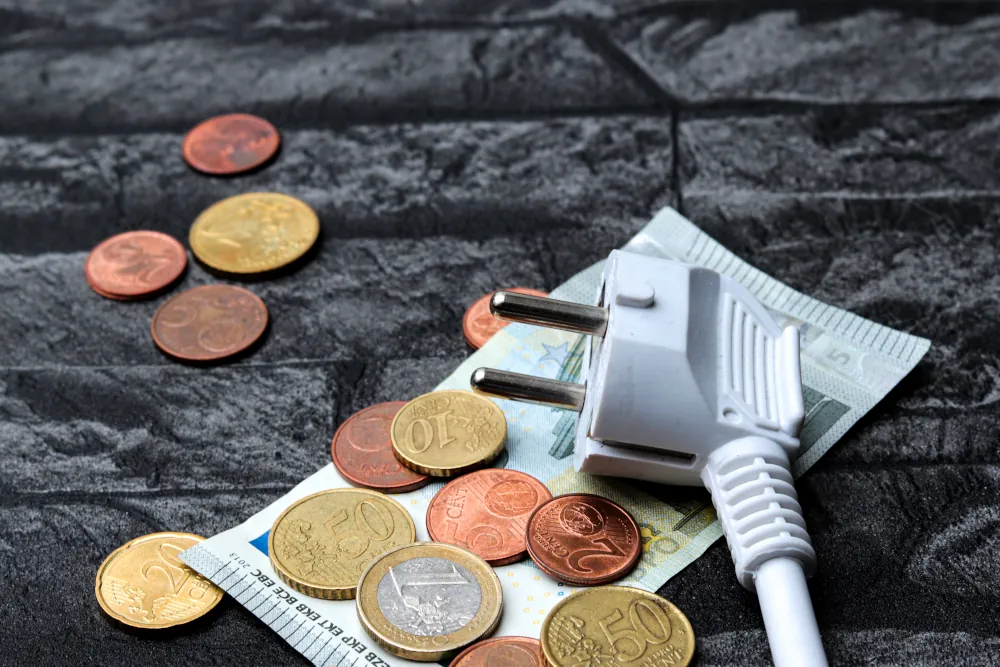 Closeup shot of a Euro banknote and coins and a white electric plug on a grey surface