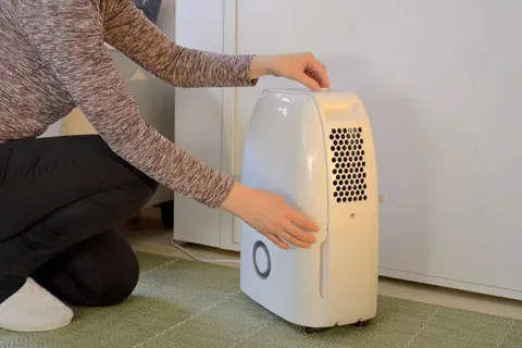 Person adjusting a portable home dehumidifier or air purifier on a tiled floor